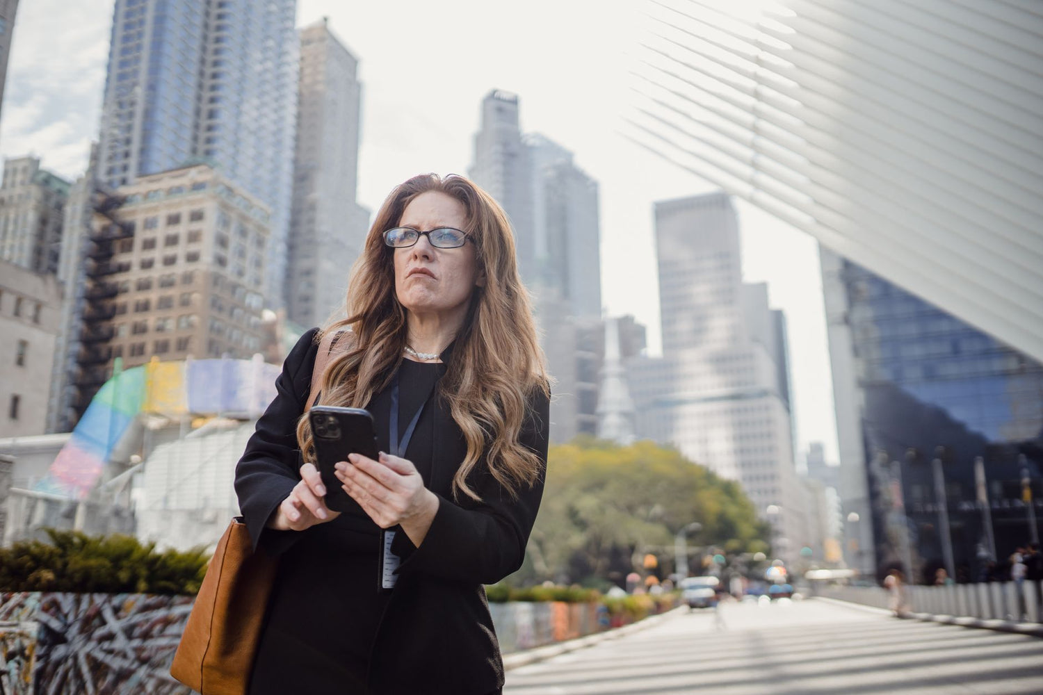 Confident woman with smartphone walking amidst modern skyscrapers. Urban business concept.